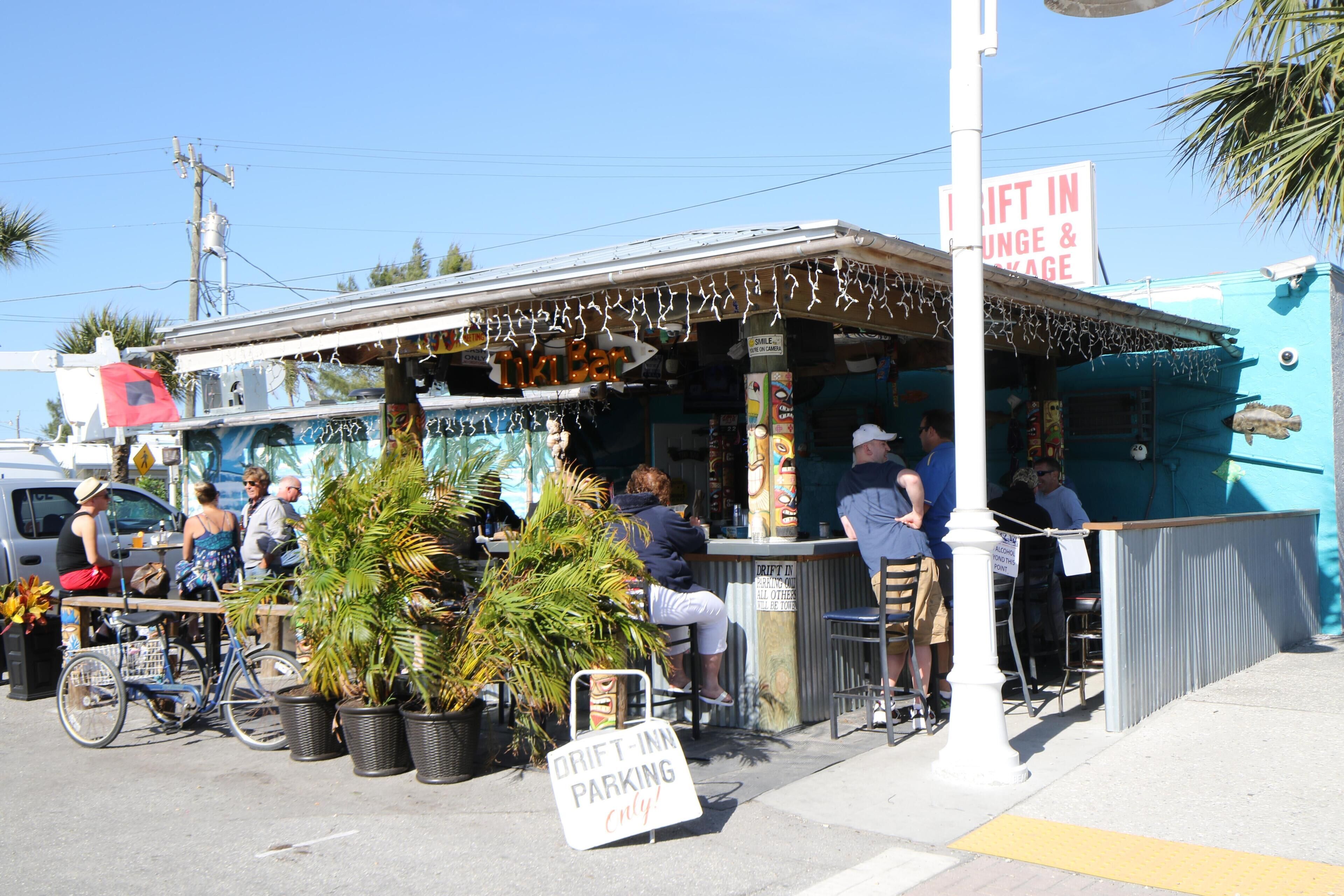 A small outdoor eatery with a bar area, seating, and a sign indicating 'DRIFT IN LUNCH & DINNER'.