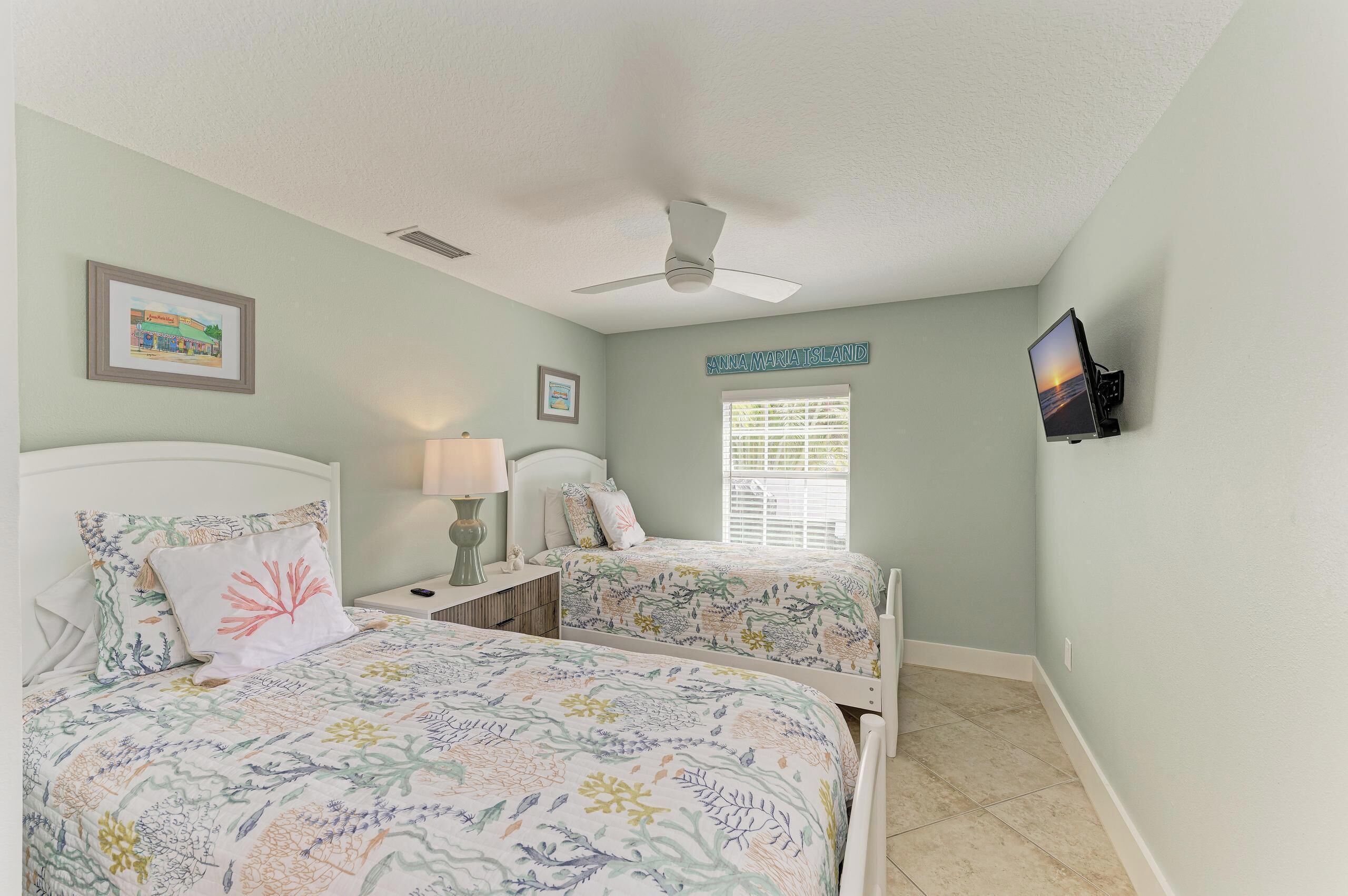 A bedroom with two beds, a ceiling fan, a TV, and a window with blinds.