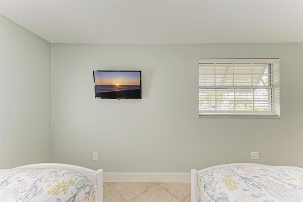 A room with two beds, a television mounted on the wall, and a window with blinds. - Anna Maria Island Blue Bella Bliss - Private Heated Pool (Holmes Beach)
