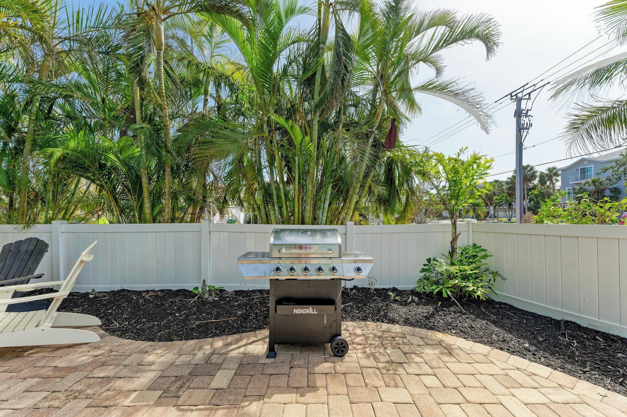 A barbecue grill with a built-in storage compartment, a white fence, and a brick patio.