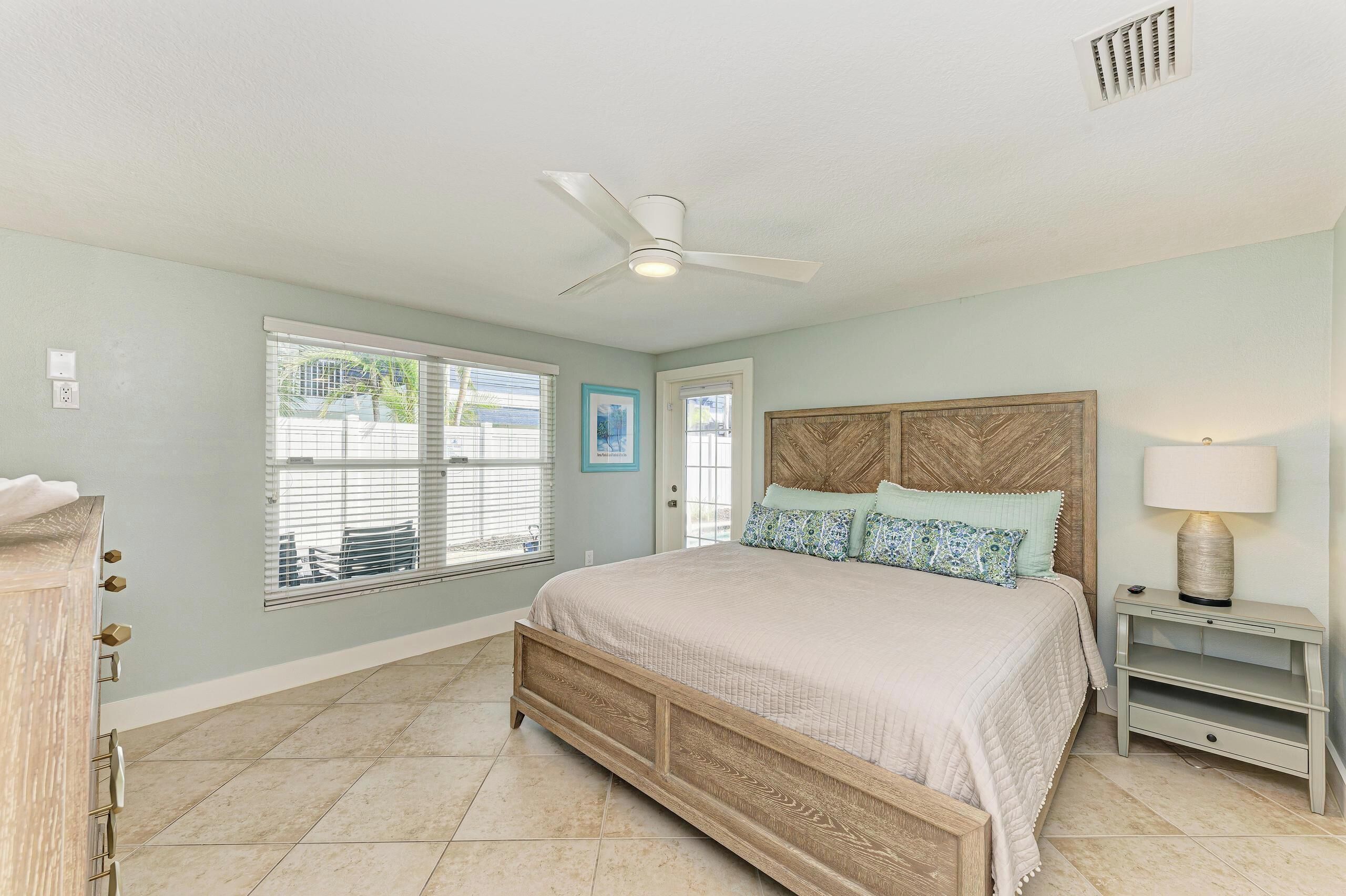 A bedroom with a bed, a nightstand, a ceiling fan, and a window with blinds.