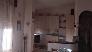 Eine kleine Küche mit Holzausstattung, einem Esstisch mit blumigem Tischläufer und einem großen Fenster mit Vorhängen.