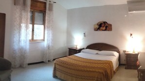 Ein Schlafzimmer mit einem Bett, zwei Nachttischen, einem Fenster mit Vorhängen, einem Wandbild und einer Klimaanlage.