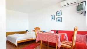 A room with a bed, a table with a checkered tablecloth, a red sofa, and a television mounted on the wall.