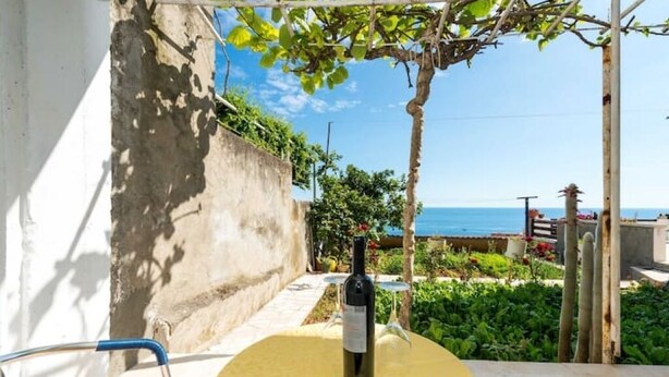A table with a bottle of wine, a chair, and a view of the sea.