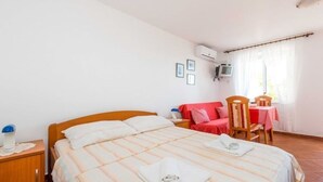 A hotel room with a bed, a small table with a red tablecloth, a chair, and a window with curtains.