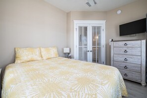 A bedroom with a bed, a dresser, a television, and a door with a window. - Sunset Island 3A Sunset Island Drive (Ocean City)