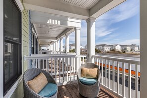 A covered porch with two wicker chairs, a white railing, and a view of residential buildings in the background. - Sunset Island 3A Sunset Island Drive (Ocean City)