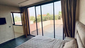 Un dormitorio moderno con una cama grande, un televisor y vistas a un jardín a través de amplios ventanales.