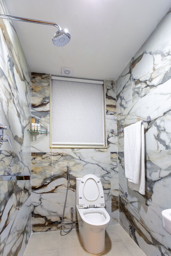Et badeværelse med marmorvæg, toilet, brusebad og håndklædestang.