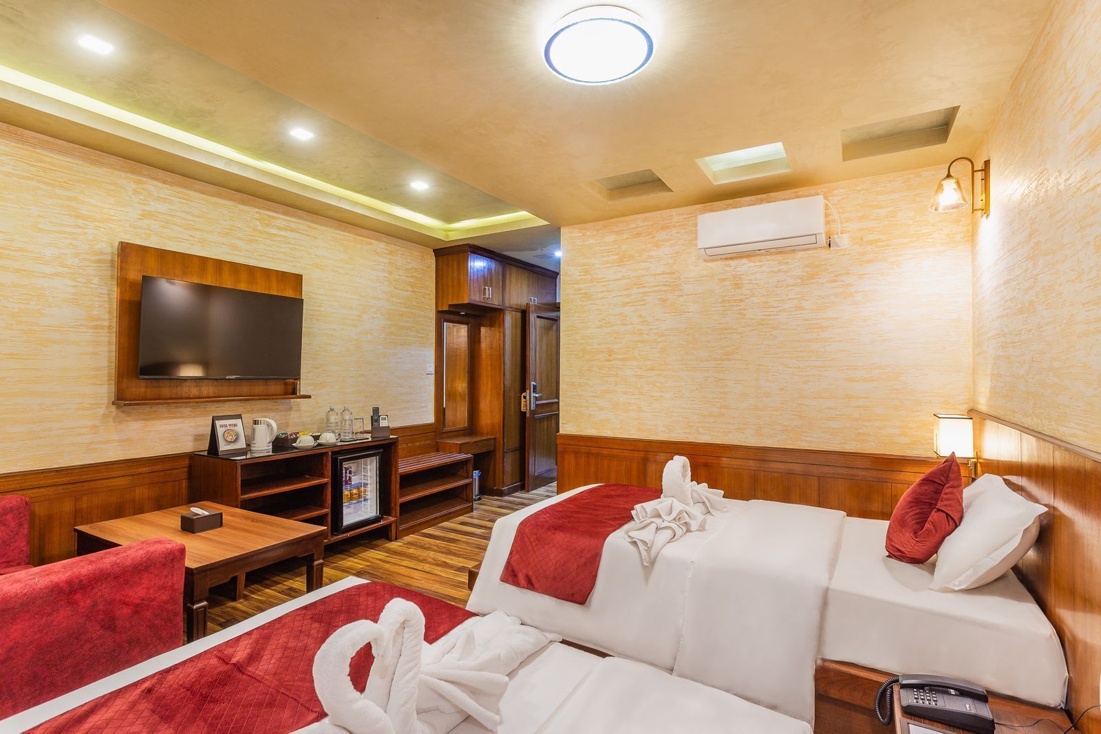 A hotel room with a TV, a desk with a coffee maker, a bed with a red blanket, and a red pillow.