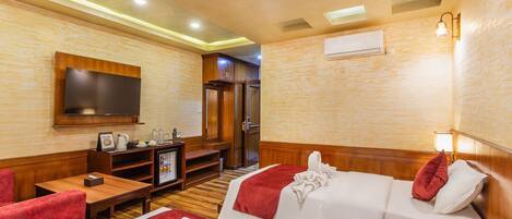 A hotel room with a TV, a desk with a coffee maker, a bed with a red blanket, and a red pillow.