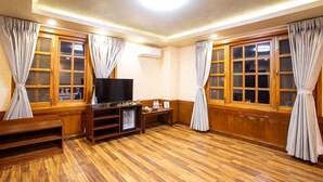 A room with wooden flooring, a television on a wooden stand, and curtains on the windows. - Hotel Nova Nook (Kathmandu)