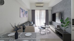 A modern living room with a sofa, a dining table set for two, a TV mounted on the wall, and an air conditioning unit. - Taipei Main Station Modern Comfort 2B1b Living, Dining, Kitchen (Taipei City)