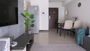 A modern living room with a flat-screen TV, a potted plant, a refrigerator, and a dining area with chairs and a table. - Taipei Main Station Modern Comfort 2B1b Living, Dining, Kitchen (Taipei City)