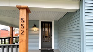 A house number 552 on a wooden post, a front door with a glass panel, and a porch with a black metal railing.