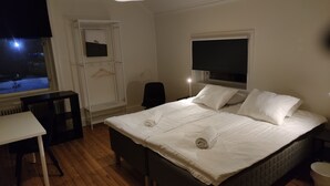 A bedroom with a bed, bedside table, chair, and a window with a view of a snowy street at night. - 11rum&kök  (Sandviken)