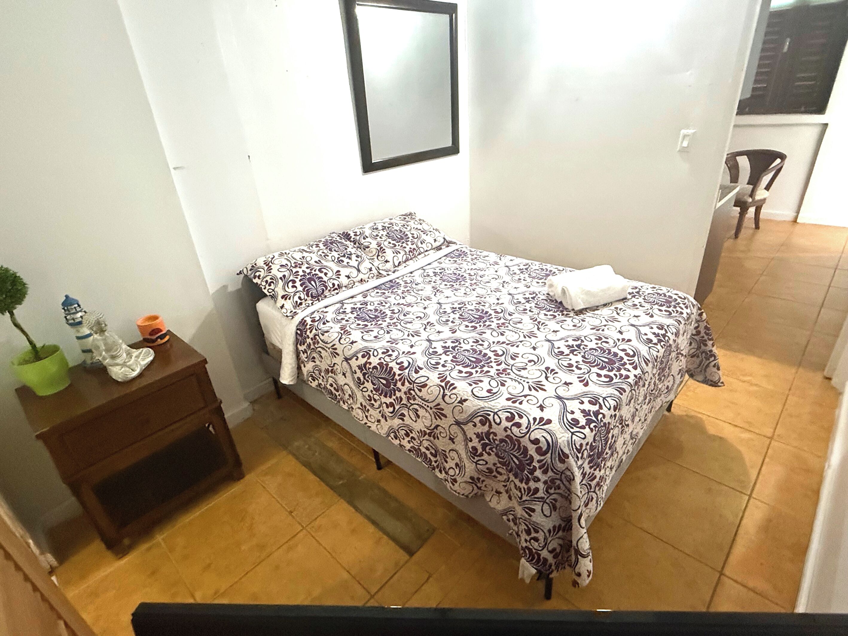 Une petite chambre à coucher, bien rangée, avec un lit, une table de chevet et une plante en pot.