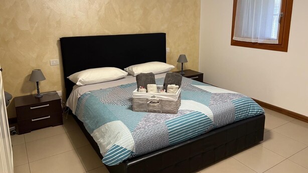 Een slaapkamer met een bed, twee nachtkastjes, een raam met gordijnen en een wand met een structuur afwerking.