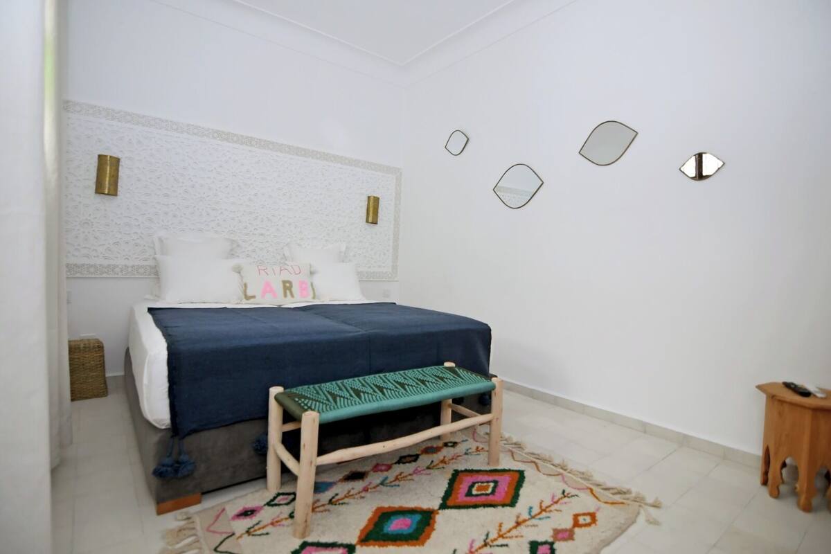 A bedroom with a bed, a bench, a patterned rug, and a small wooden stool.