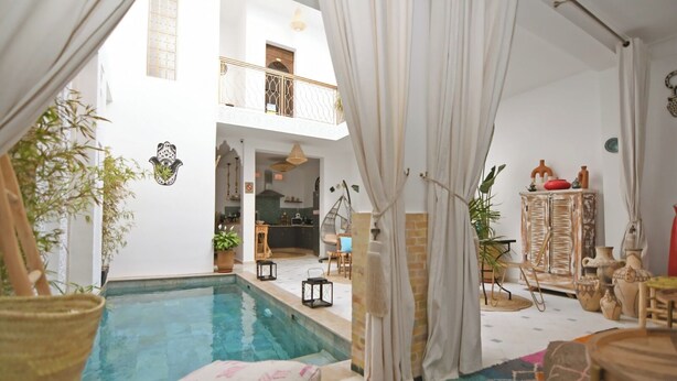 Amplia zona de piscina interior con vistas a una cocina y un salón, que incluye una silla colgante, plantas en macetas y un mueble decorativo.