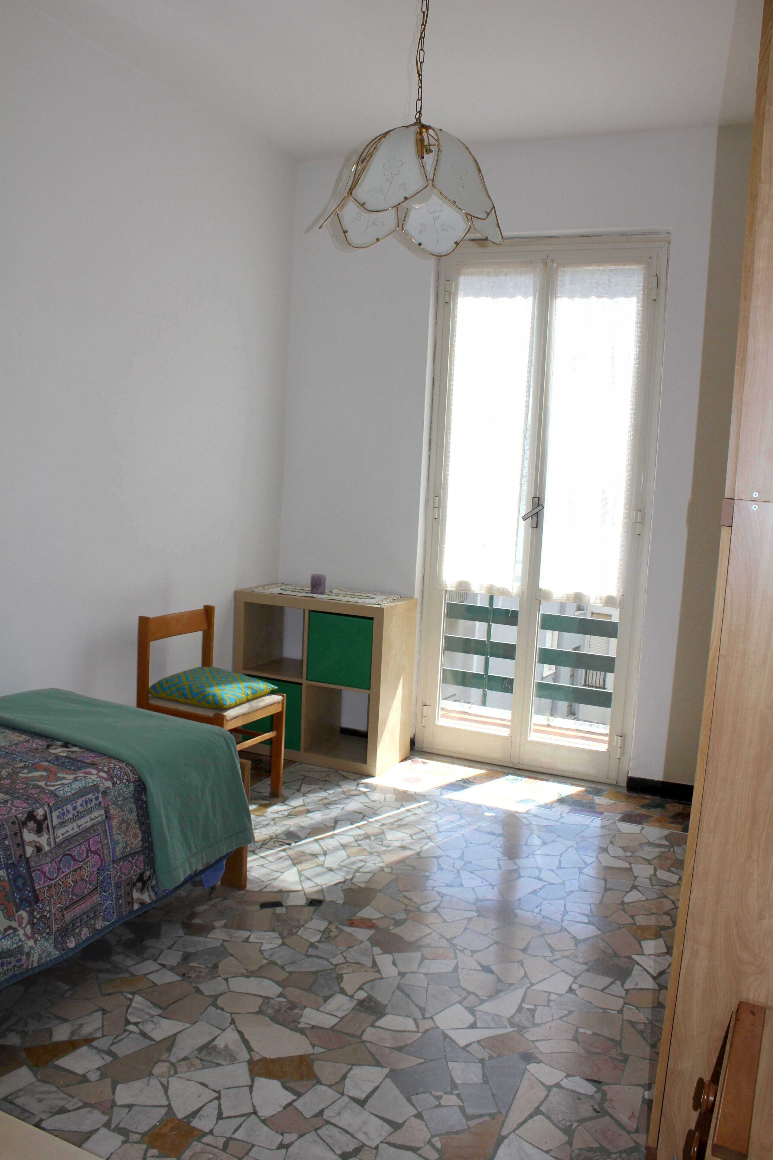 Ein Schlafzimmer mit Bett, Sessel, Schreibtisch und Balkon.