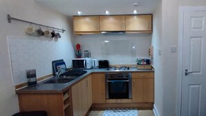 A compact kitchen with wooden cabinets, a stove, a sink, and a microwave. - Central Edinburgh Flat Sleep 6, Minutes From old Town (Edinburgh)