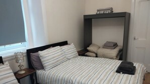 A bedroom with two beds, each with striped bedding and pillows. There is a bedside table with a lamp and a shelf above the bed. - Central Edinburgh Flat Sleep 6, Minutes From old Town (Edinburgh)