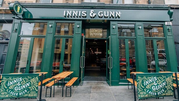 The exterior of INNIS & GUNN, featuring a green facade, wooden benches, and signs advertising lager beer and craft taps. - Central Edinburgh Flat Sleep 6, Minutes From old Town (Edinburgh)