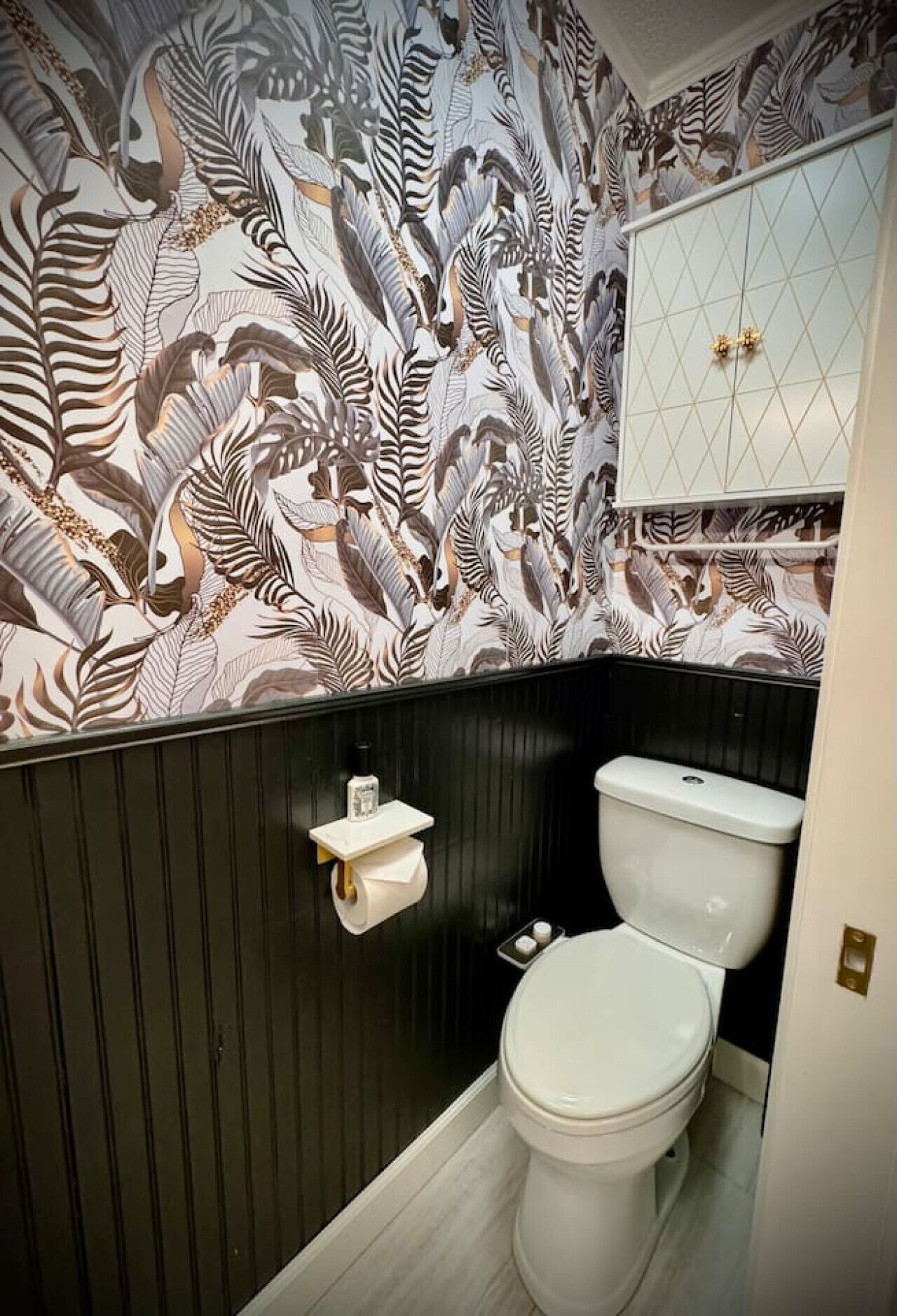 Une salle de bain avec un papier peint à rayures zébrées, des toilettes blanches et un meuble-lavabo noir doté d’un robinet doré.
