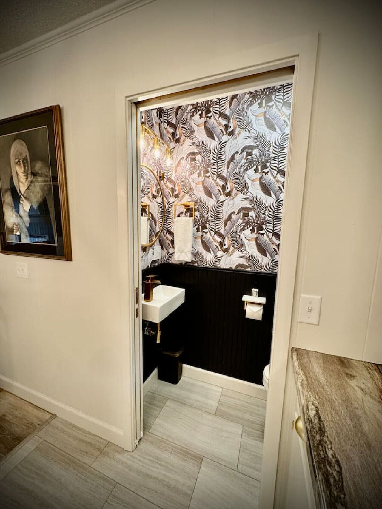 A bathroom with a black and white patterned wallpaper, a white sink, and a framed artwork on the wall.