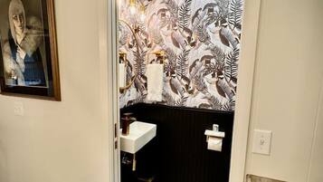 A bathroom with a black and white patterned wallpaper, a white sink, and a framed artwork on the wall.