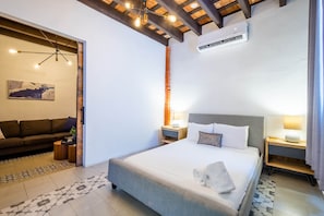 Habitación de hotel con cama, sofá, mesita de noche, lámpara y unidad de aire acondicionado.