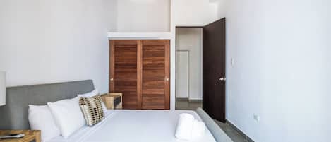 A modern bedroom with a bed, a wooden wardrobe, and a door leading to another room.