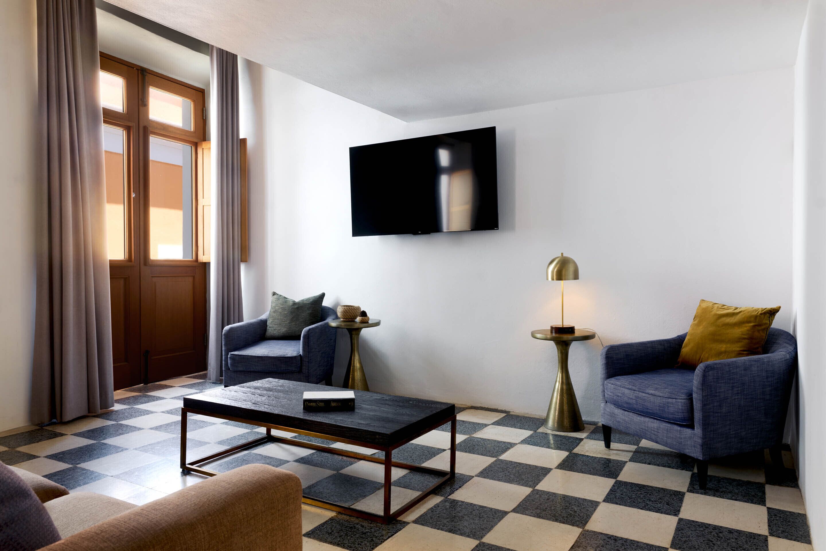 Un salon moderne avec un sol à carreaux, deux canapés, une table basse, un téléviseur à écran plat fixé au mur et une lampe sur une table d’appoint.