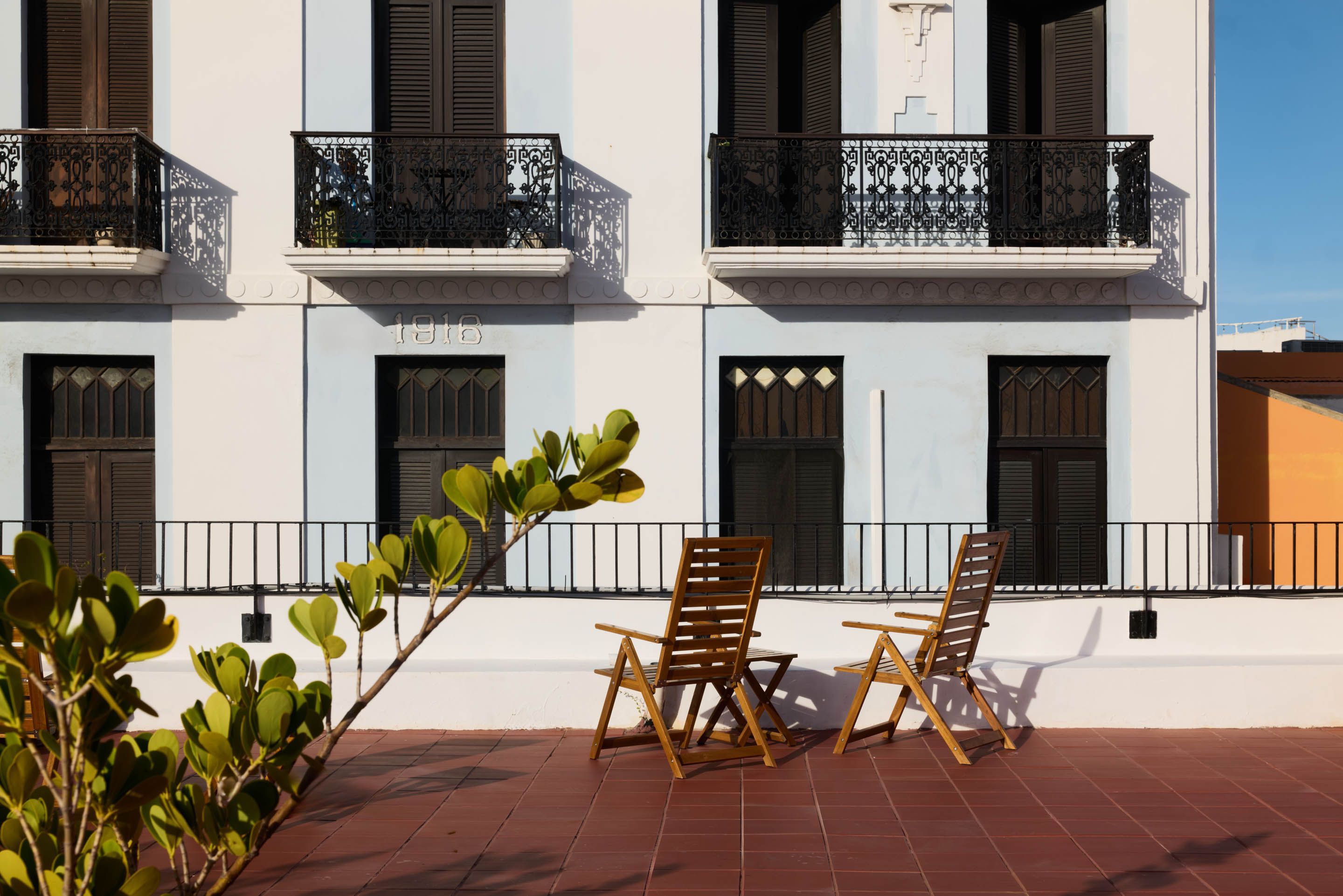 A building with balconies, a tiled patio, and two wooden chairs.