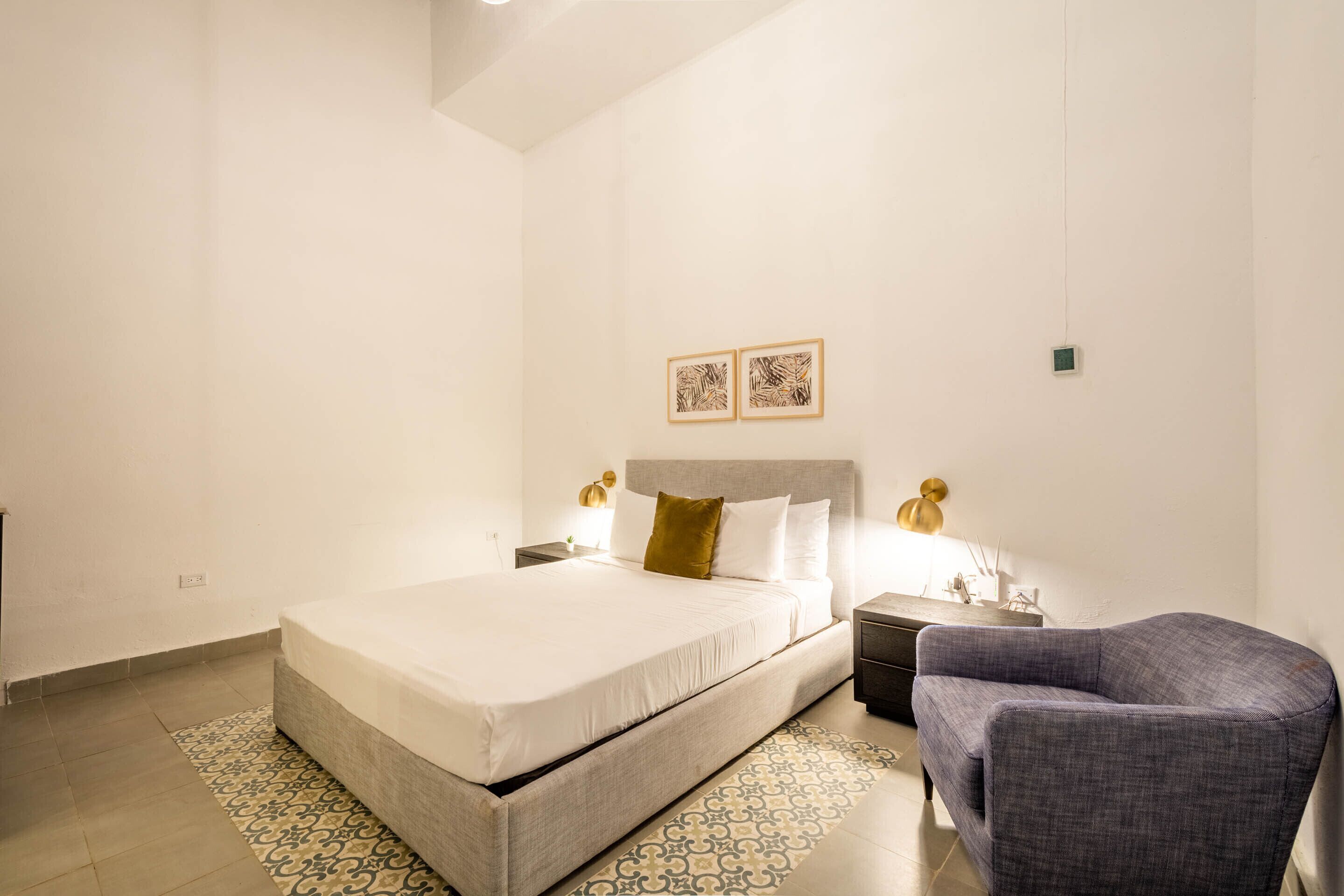 A bedroom with a bed, bedside tables, a chair, and two wall-mounted artworks.