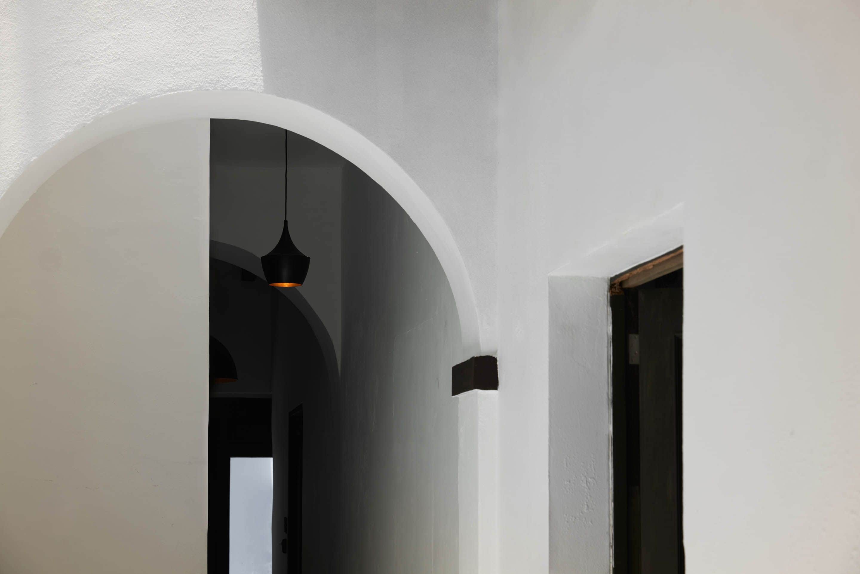 Un pasillo con pared blanca, un arco de entrada y una lámpara colgante.