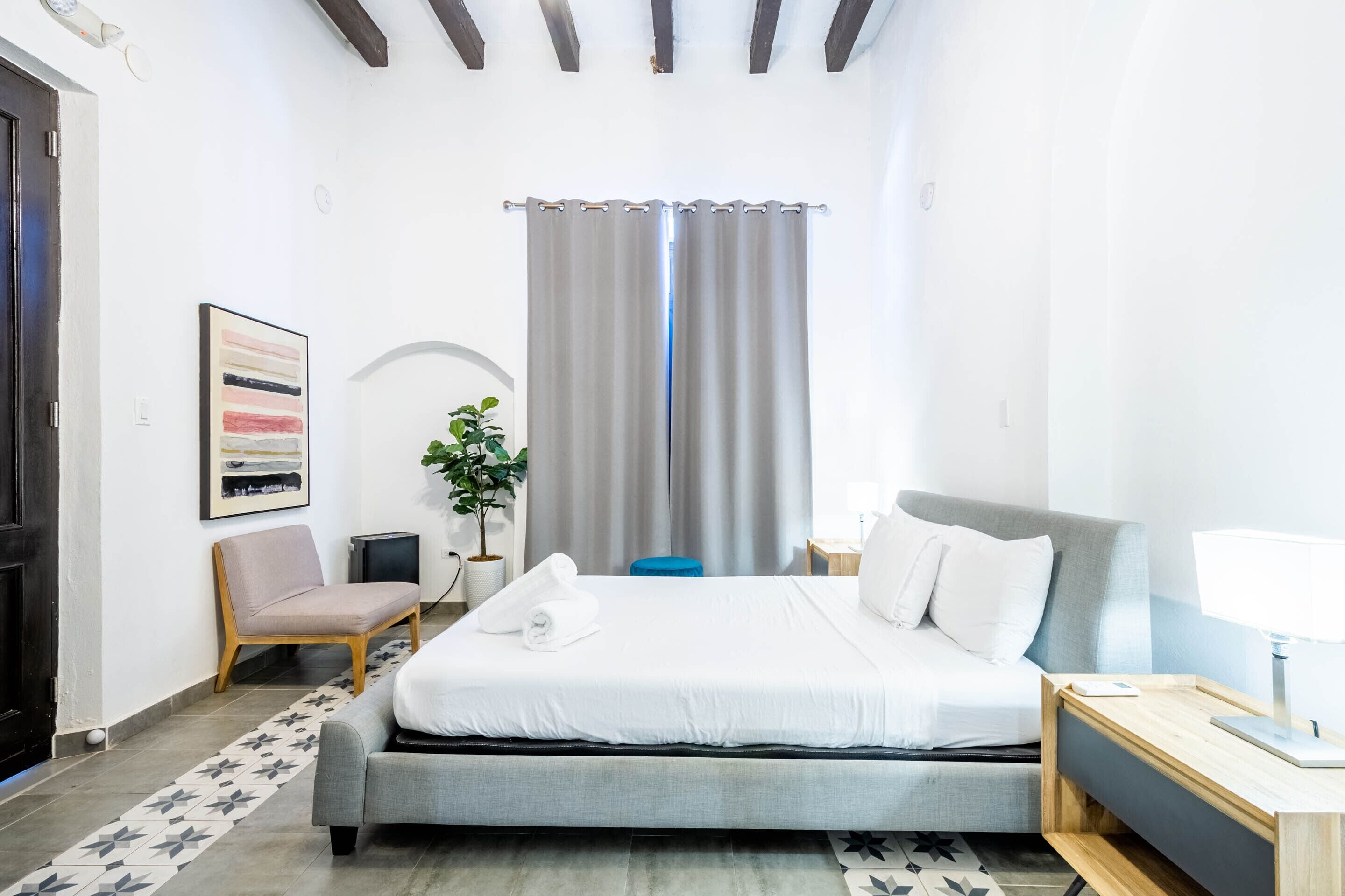 A modern hotel room with a bed, a chair, a desk, a lamp, and a potted plant.