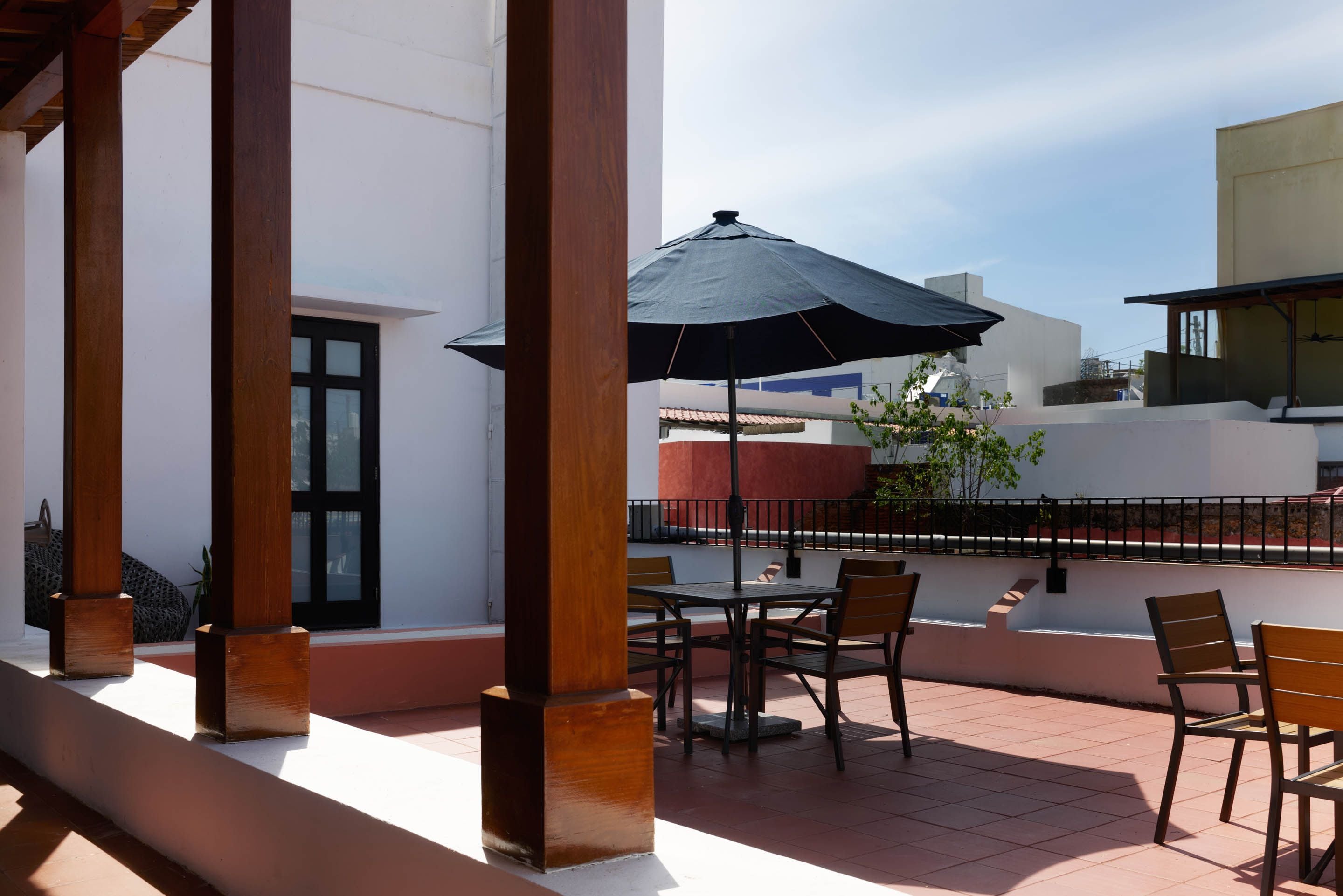 Ein Außenbereich mit Terrasse, einem Tisch, Stühlen und einem großen Sonnenschirm, mit Blick auf die umliegenden Gebäude.