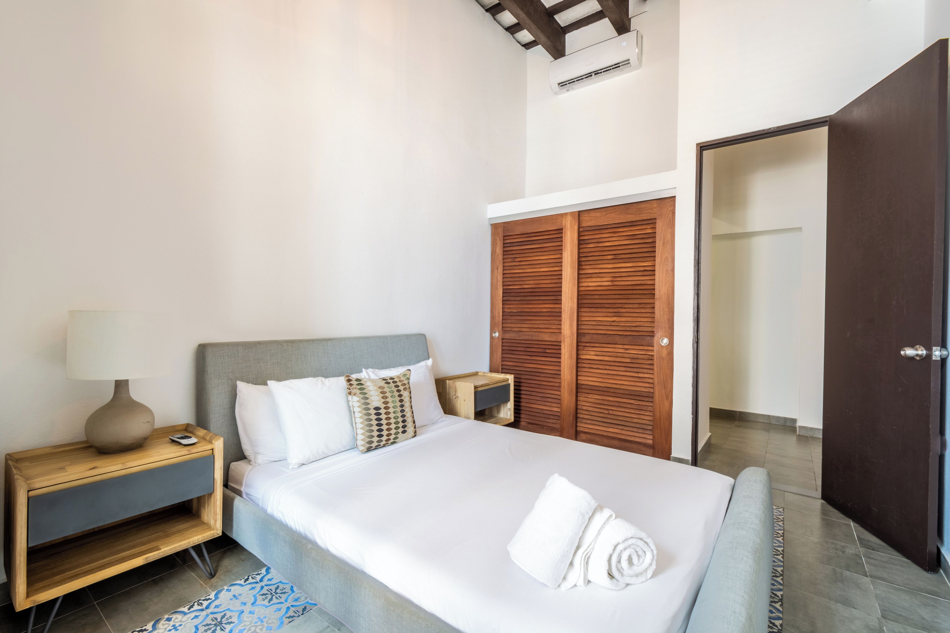 A hotel room with a bed, a nightstand, a lamp, a wooden wardrobe, and a door.