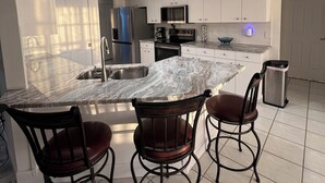 Una cocina moderna con encimera de mármol, electrodomésticos de acero inoxidable y una zona de bar con taburetes.
