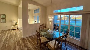 Un comedor con mesa de vidrio y sillas de madera, una araña y un ventanal con vistas al exterior.