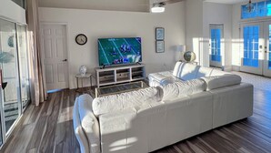 Un salón amplio con un sofá blanco grande, un televisor de pantalla plana y suelo de madera.