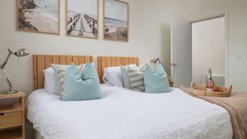 A neatly arranged bedroom with a wooden headboard, a bed with white bedding and light blue pillows, a bedside table with a lamp, and a nightstand. There are two framed pictures on the wall above the bed.