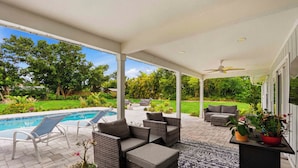 A covered patio with outdoor furniture, a pool, and a view of a lush garden. - Heated Pool · Private Fire Pit · 3 Min to Beach -Manasota Key Gem 3/3 Home (Englewood)