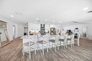 Una cocina moderna con armarios blancos, una isla central con taburetes altos y un refrigerador de acero inoxidable.