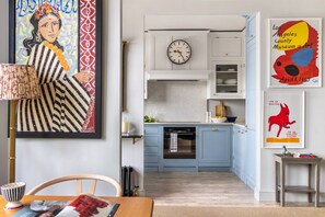 Una cocina moderna con un reloj, un comedor con mesa y sillas, y obras de arte en las paredes.