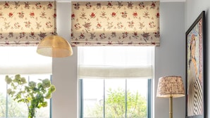 A dining area with a table, chairs, a vase with flowers, a lamp, and a window with floral curtains.