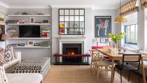 A living room with a fireplace, a television, a dining area with chairs, and a bookshelf with books.